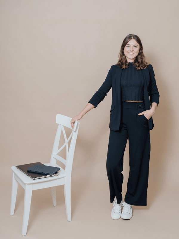 Marlene König-Kleinl in schwarzem Outfit mit Laptop und Ipad neben weißem Sessel.