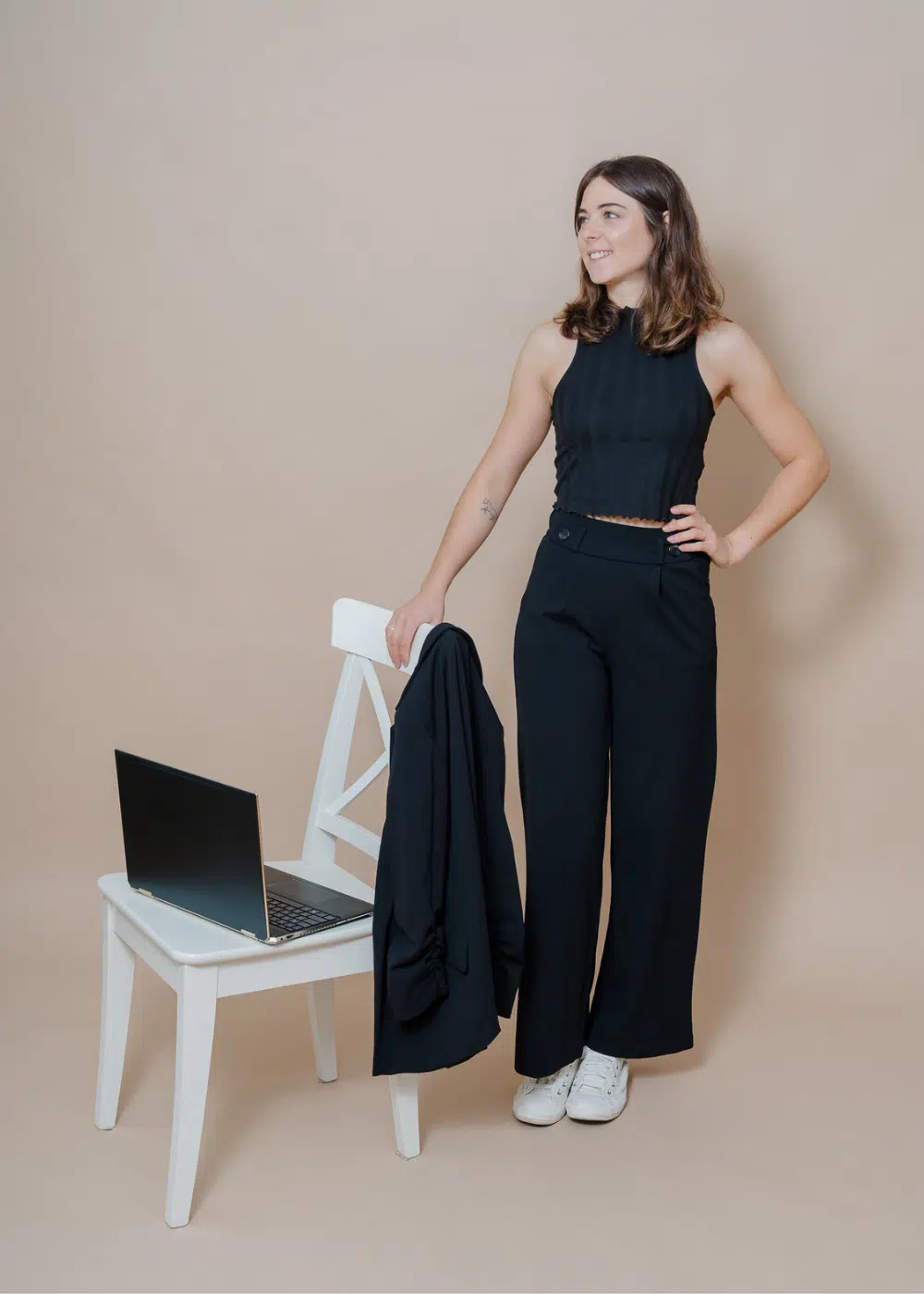 Marlene König-Kleinl in schwarzem Outfit mit Laptop und Ipad neben weißem Sessel.