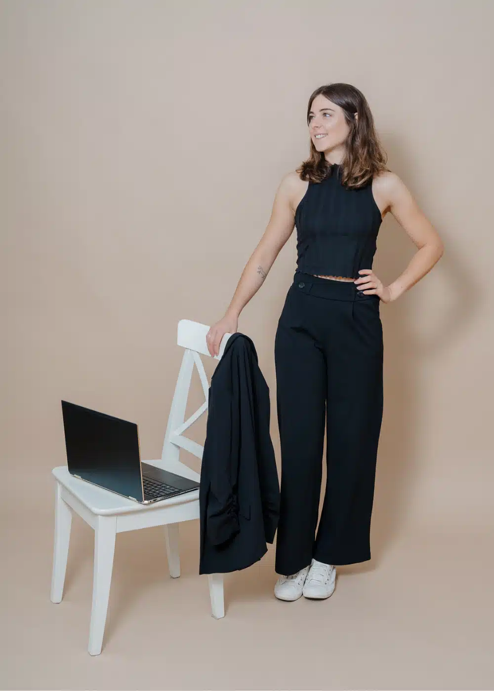 Marlene König-Kleinl in schwarzem Outfit mit Laptop und Ipad neben weißem Sessel.